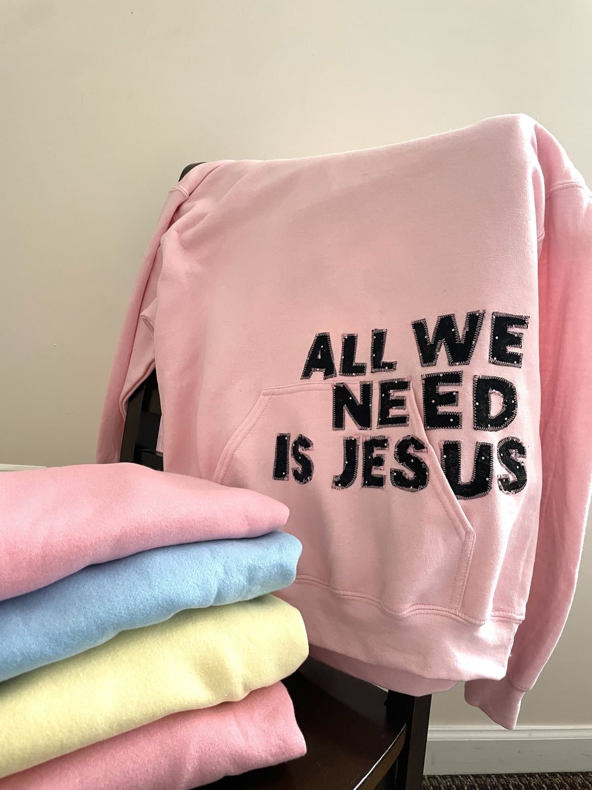 Pink hoodie with All We Need Is Jesus appliqué letters in black polka-dot fabric