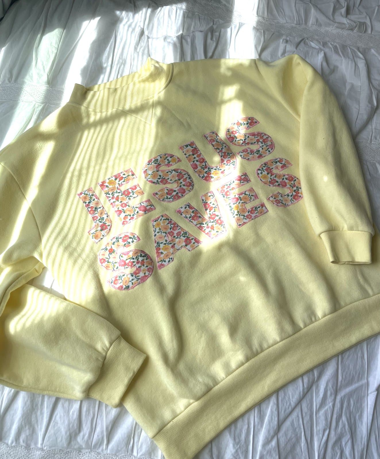 Yellow sweatshirt with floral fabric Jesus Saves appliqué, laid flat in soft natural light